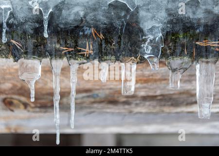 Ghiaccio su una grondaia del tetto in Finlandia con facciata in legno sullo sfondo Foto Stock