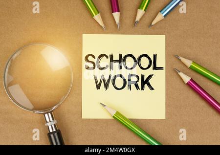 Concetto di istruzione. Sul tavolo sono presenti matite, una lente d'ingrandimento e un adesivo con l'iscrizione - lavoro scolastico Foto Stock