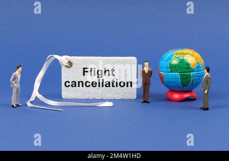 Concetto di viaggio. Sulla superficie blu ci sono figurine di persone, un globo e un piatto bianco con l'iscrizione - cancellazione del volo Foto Stock