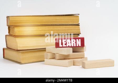 Concetto di istruzione. Su una superficie bianca, una pila di libri e blocchi di legno, su un blocco rosso c'è un'iscrizione - IMPARA Foto Stock