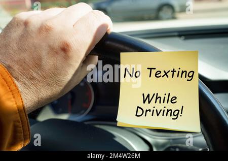 Il concetto di sicurezza dei trasporti. Un uomo tiene il volante accanto a un adesivo con la scritta "No Texting" durante la guida Foto Stock