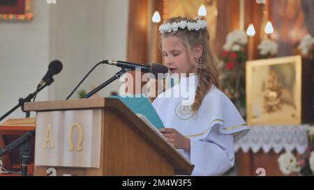 Pervomaysk, Bielorussia - 17 giugno 2022: Una ragazza legge la Bibbia alla sua prima comunione cattolica. Foto Stock