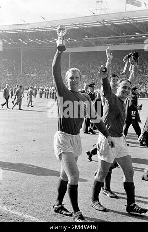 File foto datata 30-07-1966 del capitano d'Inghilterra Bobby Moore (l) mostra con orgoglio il trofeo Jules Rimet mentre lui e i compagni di squadra Gordon Banks (c) e George Cohen (r) sfilano il trofeo intorno a Wembley. L'ex difensore dell'Inghilterra e di Fulham George Cohen è morto all'età di 83 anni. Data di emissione: Venerdì 23 dicembre 2022. Foto Stock