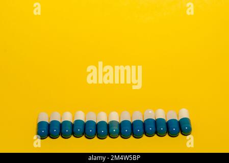 Un primo piano di pillole bianche e blu, e farmaci su sfondo giallo Foto Stock
