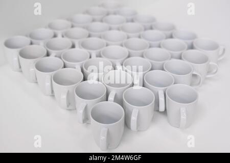 File di tazze bianche vuote a forma di diamante su sfondo bianco. Vista dall'alto, concentratevi sulle tazze anteriori, sbiadendo verso la parte posteriore Foto Stock