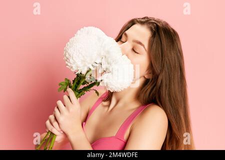 Ritratto di bella giovane ragazza in costume carino posa con fiori bianchi su sfondo rosa. Odore perfetto Foto Stock