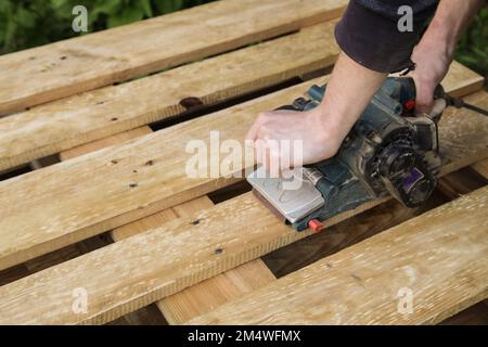 Lavorazione tavole di legno a mani maschili, pallet con levigatrice Foto Stock