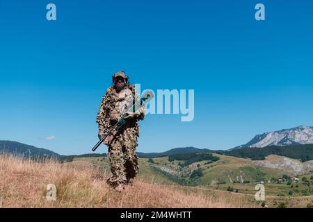 Soldato dell'esercito che tiene in mano un fucile da cecchino con portata e camminando nella foresta. guerra, esercito, tecnologia e concetto di persone. Foto Stock