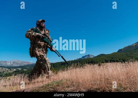 Soldato dell'esercito che tiene in mano un fucile da cecchino con portata e camminando nella foresta. guerra, esercito, tecnologia e concetto di persone. Foto Stock