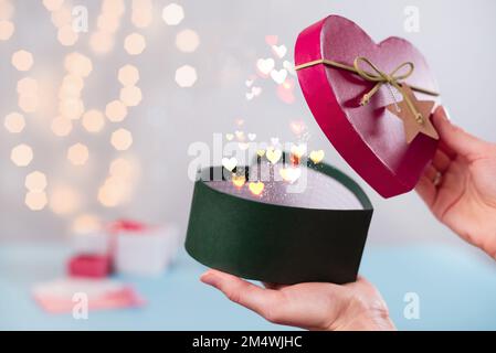 Magia per St. San Valentino, regali a forma di cuore in scatola aperta in mano. Copia spazio per messaggio d'amore. Scegli il regalo di Natale per la persona amata Foto Stock