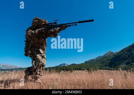 Soldato dell'esercito che tiene in mano un fucile da cecchino con portata e camminando nella foresta. guerra, esercito, tecnologia e concetto di persone. Foto Stock