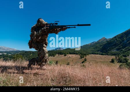 Soldato dell'esercito che tiene in mano un fucile da cecchino con portata e camminando nella foresta. guerra, esercito, tecnologia e concetto di persone. Foto Stock