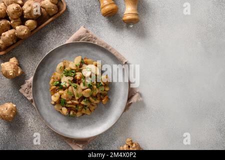 Radice di topinambur fresca arrosto, sunchiofi con aglio e prezzemolo su fondo grigio. Vista dall'alto. Spazio di copia. Foto Stock