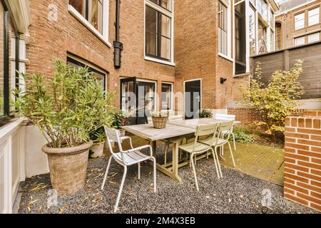 un patio con sedie, tavolo e piante in vaso sul terreno di fronte ad una parete di mattoni che è stato dipinto di rosso Foto Stock