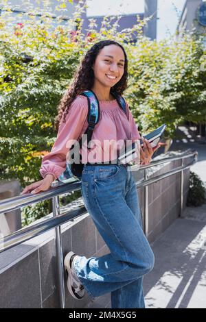 Primo piano felice giovane studentessa nera che tiene i suoi libri nel campus. Fiducia in se stessi Foto Stock