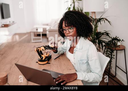 Progettare utilizzando un computer portatile che tiene il modello di robot alla scrivania in ufficio Foto Stock