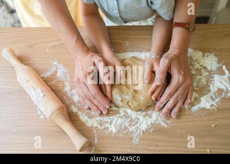 Mani di donna che impastano l'impasto dei biscotti sul tavolo a casa Foto Stock