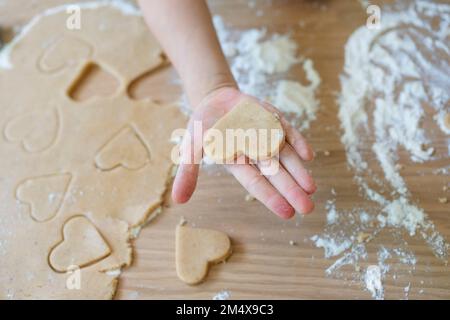 Mano della ragazza che tiene la pasta del biscotto a forma di cuore sul tavolo nel paese Foto Stock