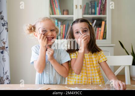 Ragazze che guardano attraverso la taglierina di biscotto a forma di cuore nel paese Foto Stock