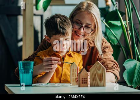 Madre e figlio felice pittura case modello in legno a tavola Foto Stock
