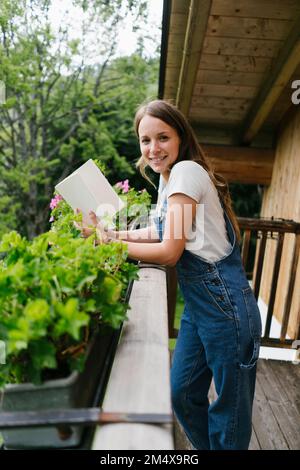 Donna sorridente con libro appoggiato su ringhiera sul balcone Foto Stock