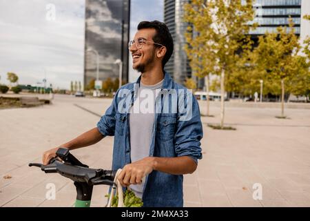 Felice giovane uomo con lo scooter elettrico a spinta in piedi sul sentiero Foto Stock