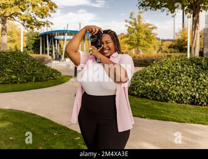 Felice giovane donna che fotografa attraverso la macchina fotografica al parco Foto Stock