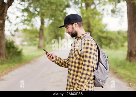 Uomo che indossa il cappuccio con uno smartphone su strada Foto Stock