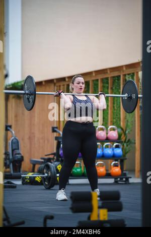 Determinata giovane donna che solleva il barbell in palestra Foto Stock