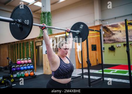 Giovane donna con le braccia sollevate sollevamento Barbell in palestra Foto Stock