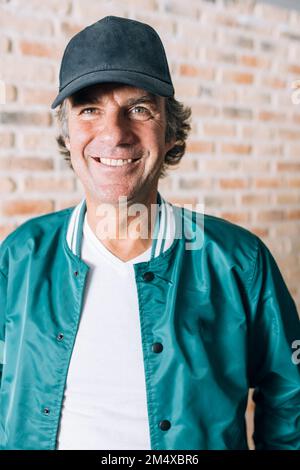 Felice uomo maturo che indossa il cappuccio di fronte al muro di mattoni Foto Stock