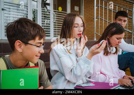 Ragazza adolescente che fa trucco con gli amici seduti sui passi Foto Stock