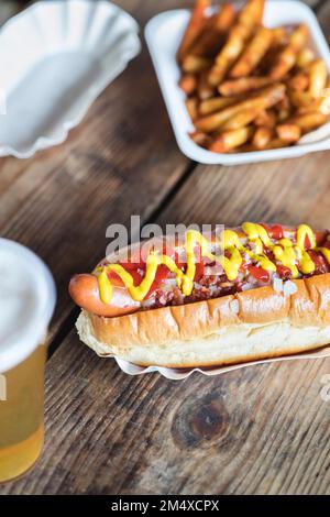 Senape e ketchup su hot dog con patatine fritte al tavolo Foto Stock