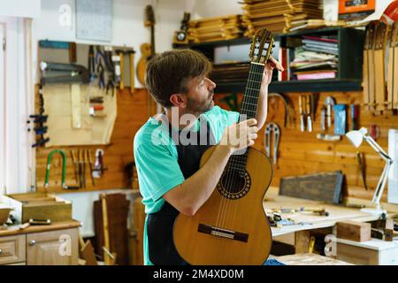 Artigiano maturo che regola la corda di chitarra in officina Foto Stock