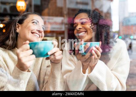 Donne felici che gustano il caffè nel caffè visto attraverso il vetro Foto Stock
