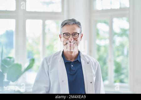 Felice medico maturo indossando occhiali in piedi nella pratica medica Foto Stock