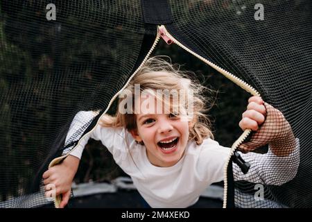 Ragazza felice che guarda attraverso la rete sul trampolino in giardino Foto Stock