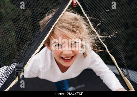 Ragazza cute felice che guarda attraverso la rete sul trampolino in giardino Foto Stock