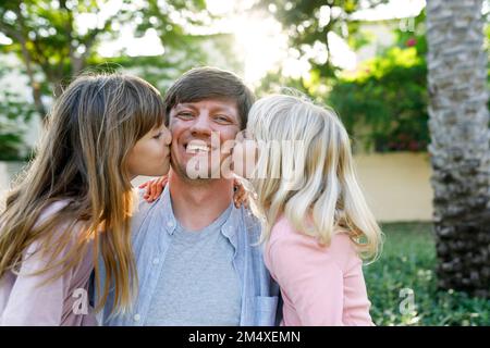 Felice padre con le figlie che lo baciano sulle guance al parco Foto Stock