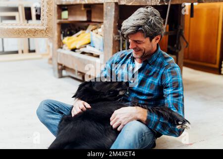 Cane sdraiato sul grembo dell'uomo in officina Foto Stock