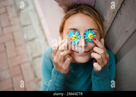 Giovane donna sorridente che tiene il fiore artificiale sopra gli occhi Foto Stock