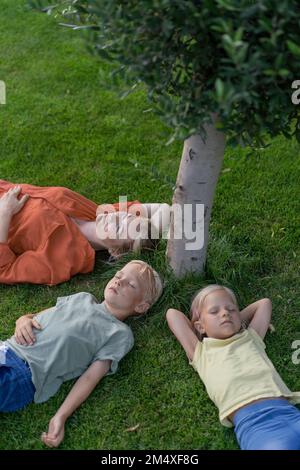 Bambini con gli occhi chiusi sdraiati da madre sull'erba Foto Stock