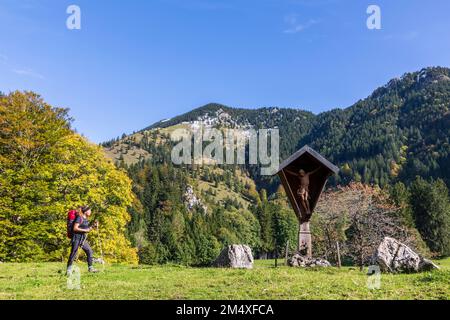 Germania, Baviera, escursionista femminile a piedi verso il santuario lungo la strada nelle Alpi Chiemgau Foto Stock