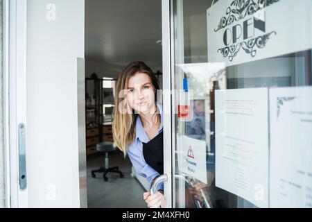 Sorridente parrucchiere che scava dalla porta del salone Foto Stock