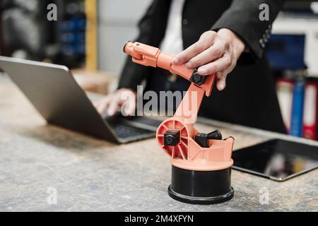 Donna d'affari che esamina il braccio robotico e che utilizza il notebook nel settore Foto Stock