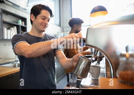 Barista sorridente che prepara il latte al bar Foto Stock