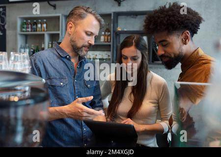 Proprietario di un caffè che condivide il tablet PC con i baristi nel bar Foto Stock
