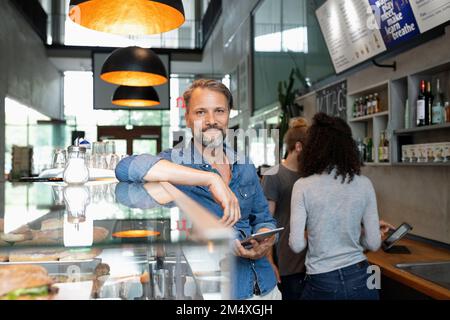 Sorridente proprietario di un bar in piedi con un tablet PC nel bar Foto Stock