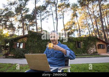 Uomo maturo che beve caffè e usa il notebook all'aperto Foto Stock