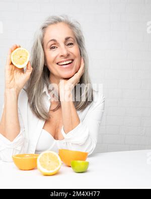 Donna felice seduta con arance e limoni al tavolo di fronte al muro Foto Stock